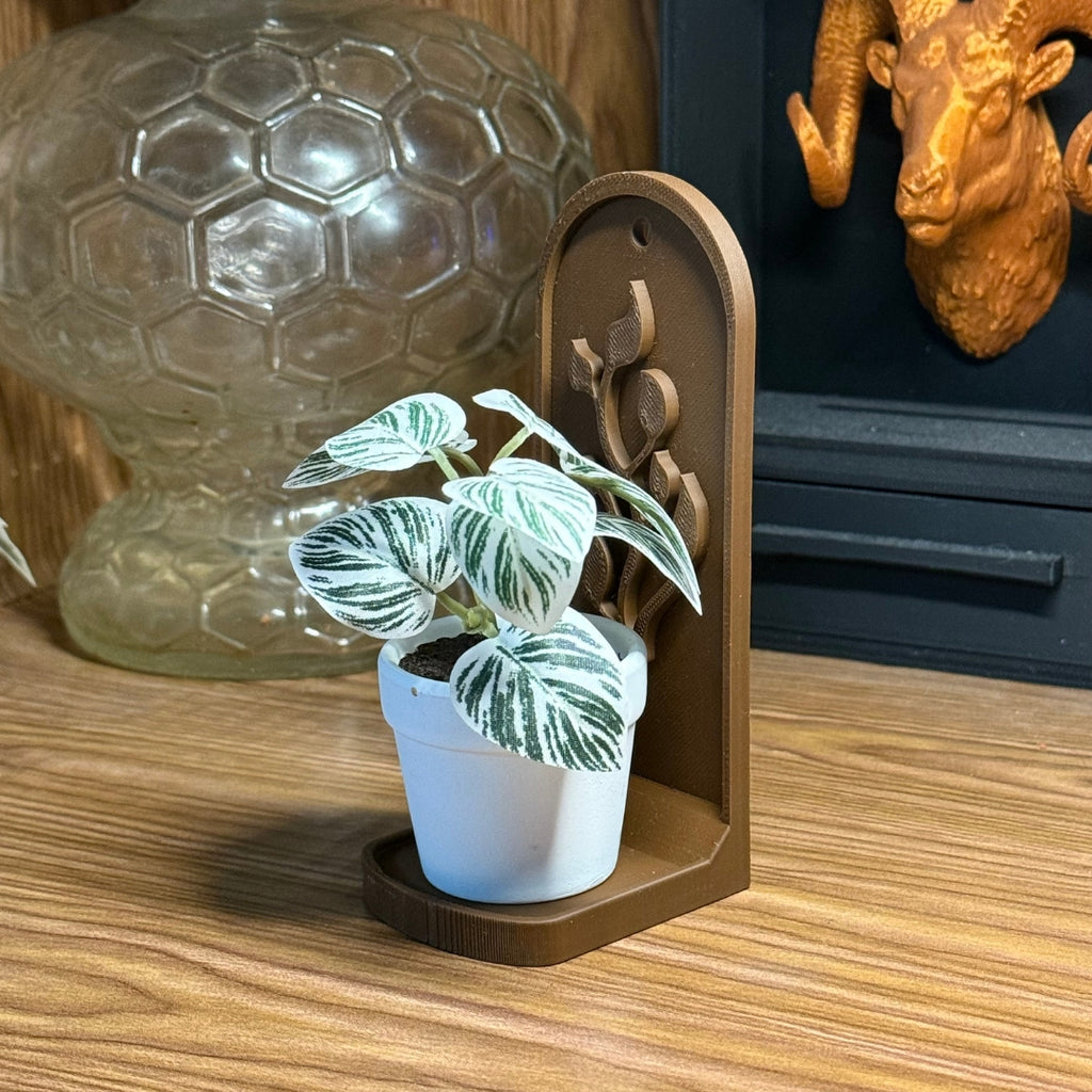 Small potted plant in a decorative wooden holder on a wooden surface with a glass ball and ram head sculpture in the background.