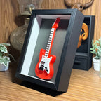 Red electric guitar model in a black display box on a wooden surface.