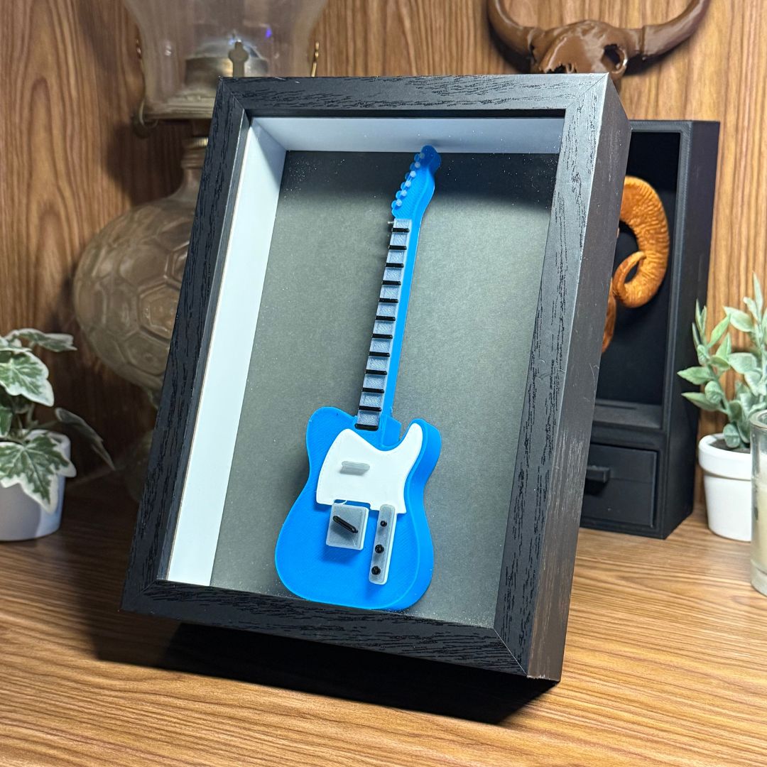 Blue and white guitar-shaped object in a black frame on a wooden surface.