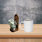 White mug with a plant on a wooden surface against a gray textured wall.