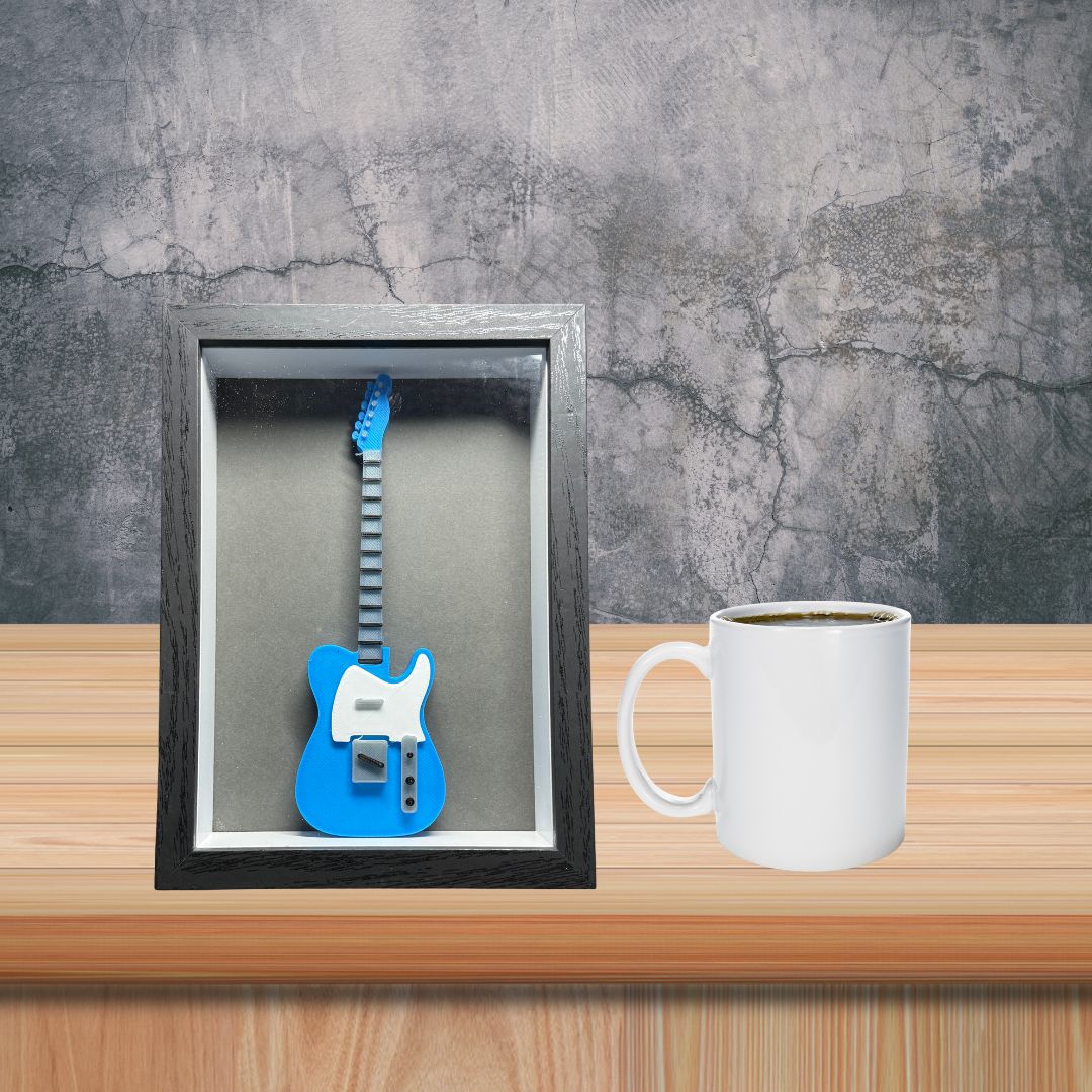 Blue guitar model in a black frame on a wooden surface with a white mug.