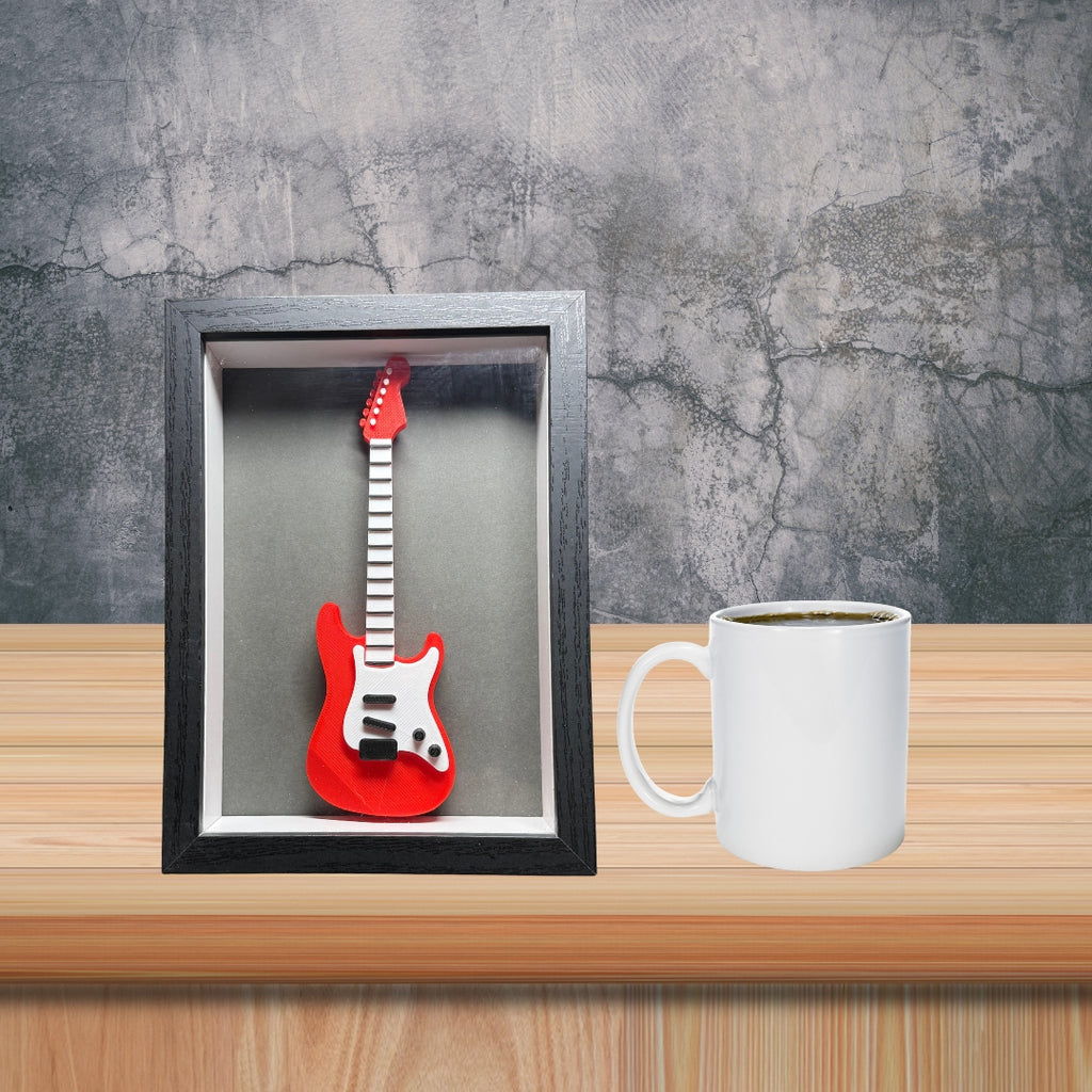 Red electric guitar in a black frame on a wooden surface with a white mug.
